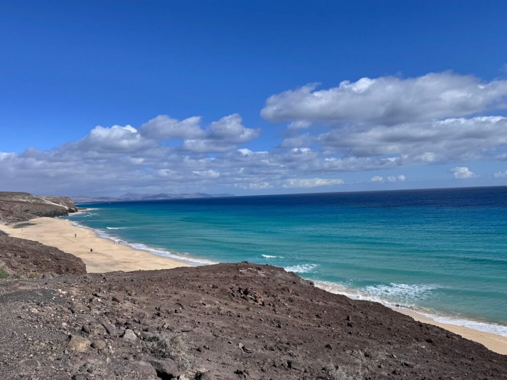 Sandstrand und türkisfarbenes Meer unter einem steinigen Vulkanhang auf Fuerteventura