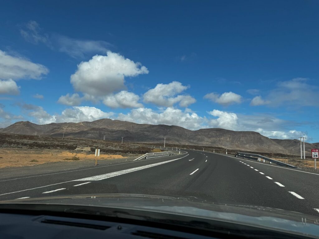 Landstraße durch die kargen Vulkanberge Fuerteventuras unter Wolkenhimmel