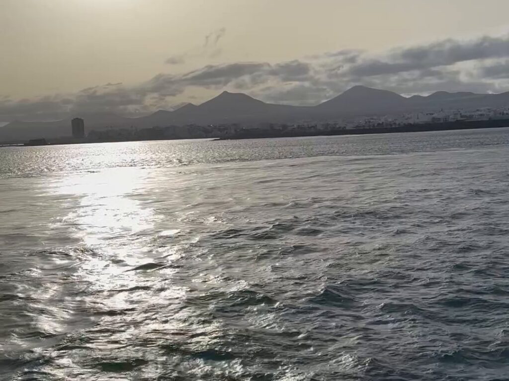Blick von der Fähre auf Arrecife auf Lanzarote bei tiefer Sonne, davor glitzerndes Meer